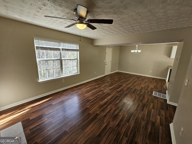 empty room featuring ceiling fan with notable chandelier, a textured ceiling, and dark wood-type flooring