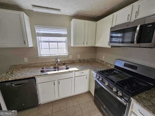 kitchen featuring appliances with stainless steel finishes, light stone countertops, light tile patterned floors, white cabinets, and sink