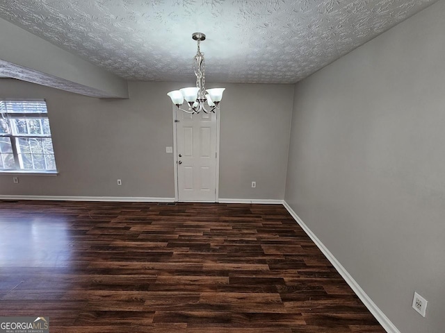 interior space featuring dark wood-type flooring, a textured ceiling, and an inviting chandelier