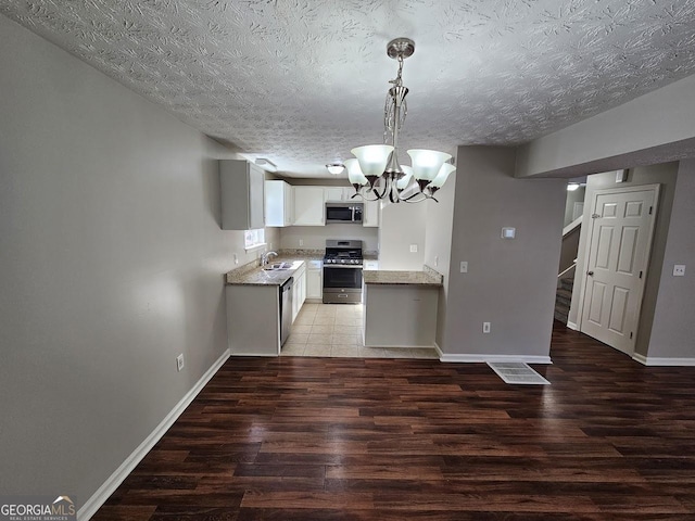 kitchen featuring hardwood / wood-style flooring, decorative light fixtures, a notable chandelier, white cabinetry, and appliances with stainless steel finishes