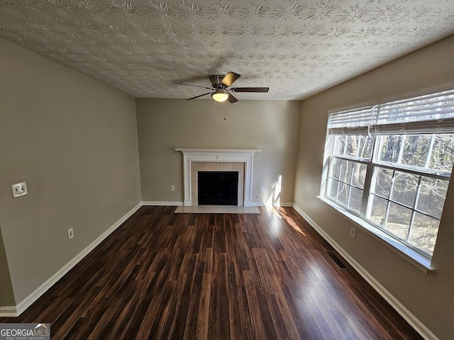 unfurnished living room featuring a tiled fireplace, a textured ceiling, a healthy amount of sunlight, and dark hardwood / wood-style floors