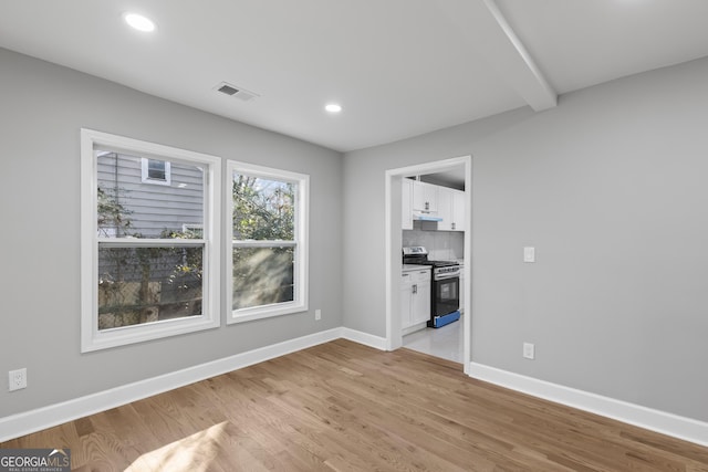 unfurnished living room featuring beamed ceiling and light hardwood / wood-style flooring