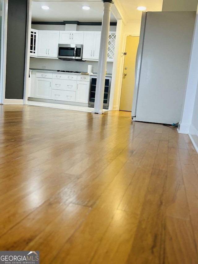 kitchen with white cabinets, ornamental molding, light hardwood / wood-style floors, white fridge, and beverage cooler