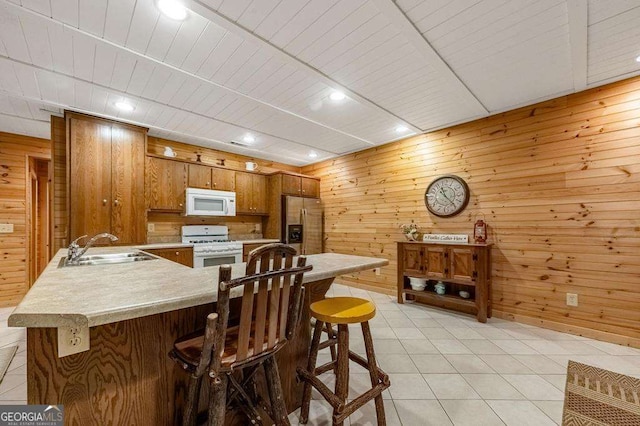 kitchen with a breakfast bar, wood walls, sink, and white appliances