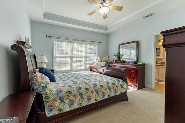 bedroom with a raised ceiling, crown molding, ensuite bath, ceiling fan, and light colored carpet