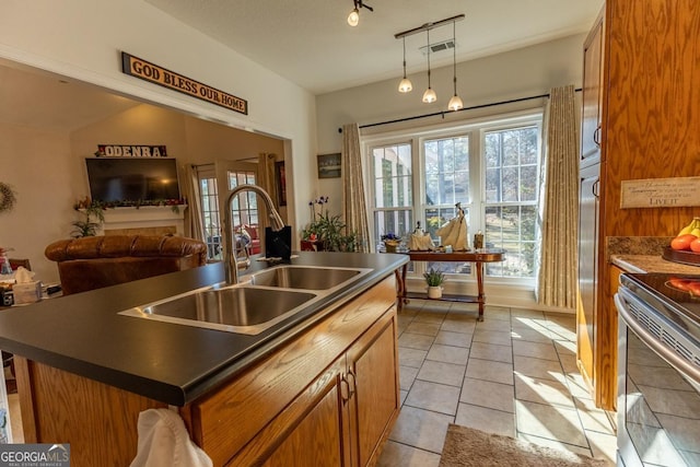 kitchen featuring sink, stove, decorative light fixtures, a center island with sink, and light tile patterned floors