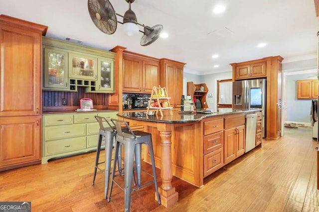 kitchen with a kitchen breakfast bar, ceiling fan, an island with sink, and light hardwood / wood-style flooring