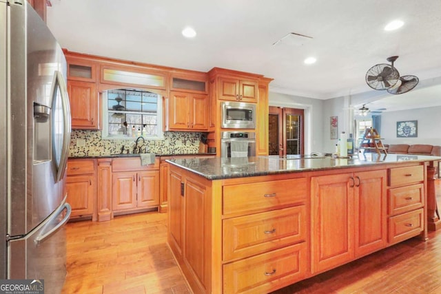 kitchen with ceiling fan, a center island, light hardwood / wood-style flooring, decorative backsplash, and appliances with stainless steel finishes