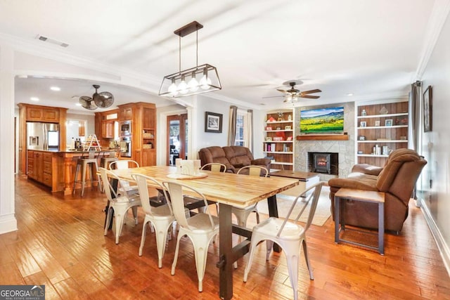 dining room featuring ceiling fan, a stone fireplace, built in features, and ornamental molding