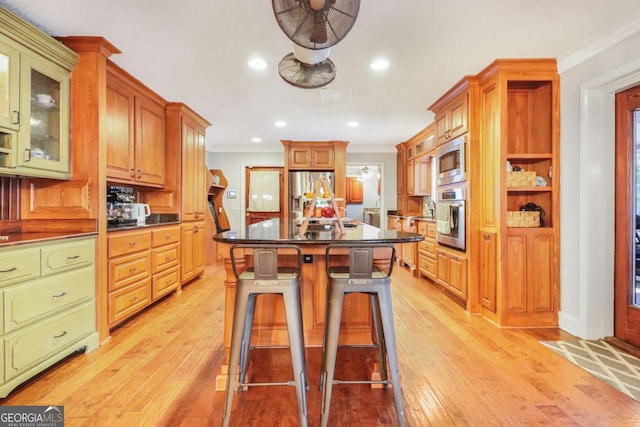 kitchen featuring appliances with stainless steel finishes, light wood-type flooring, a kitchen breakfast bar, ornamental molding, and a kitchen island