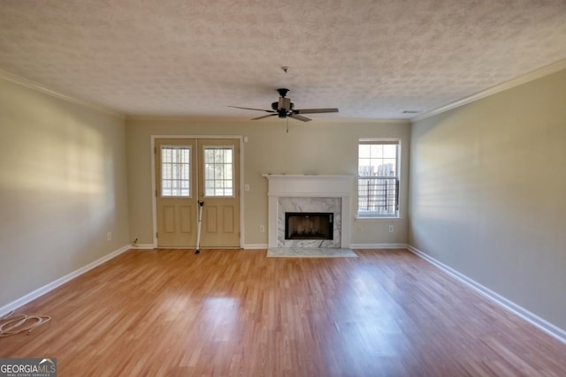 unfurnished living room with ceiling fan, a high end fireplace, light hardwood / wood-style floors, a textured ceiling, and ornamental molding