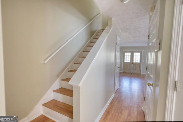 stairway with french doors and wood-type flooring