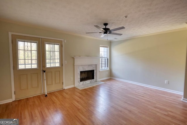 unfurnished living room with ceiling fan, a high end fireplace, crown molding, light hardwood / wood-style floors, and a textured ceiling