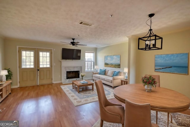 living room with ornamental molding, a textured ceiling, ceiling fan with notable chandelier, a premium fireplace, and light hardwood / wood-style floors