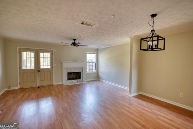 unfurnished living room featuring a fireplace, ornamental molding, ceiling fan with notable chandelier, and light wood-type flooring