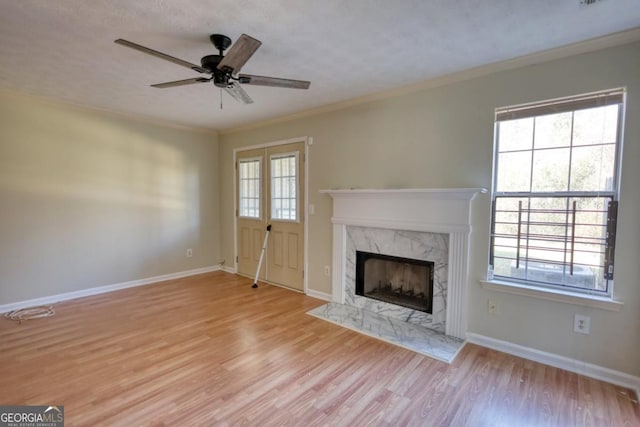 unfurnished living room featuring ceiling fan, a premium fireplace, light hardwood / wood-style flooring, a textured ceiling, and ornamental molding