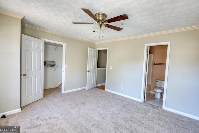 unfurnished bedroom with a walk in closet, ensuite bathroom, a textured ceiling, ceiling fan, and crown molding