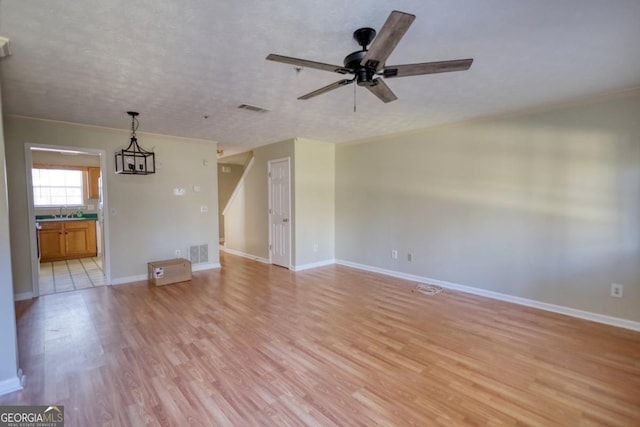 unfurnished living room with sink, ceiling fan with notable chandelier, a textured ceiling, and light wood-type flooring