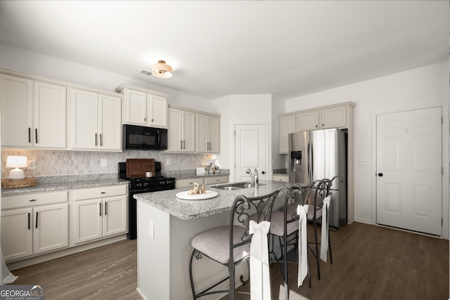 kitchen featuring a kitchen island with sink, black appliances, sink, light stone countertops, and a breakfast bar area