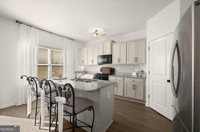 kitchen featuring a kitchen island with sink, dark wood-type flooring, black appliances, light stone countertops, and a kitchen bar