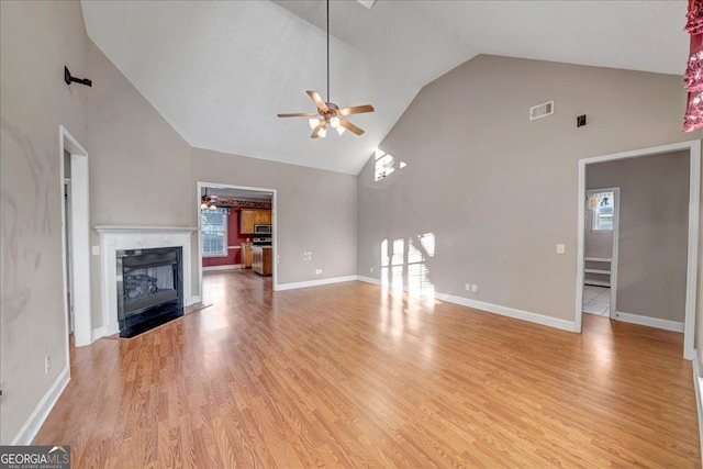 unfurnished living room with high vaulted ceiling, a high end fireplace, ceiling fan, and light hardwood / wood-style flooring