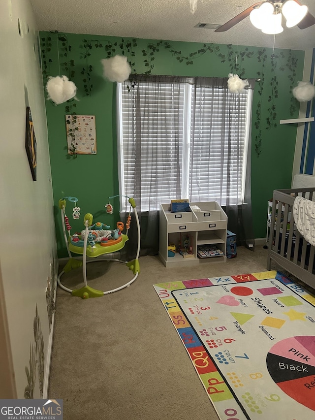 carpeted bedroom featuring a textured ceiling, ceiling fan, and a nursery area