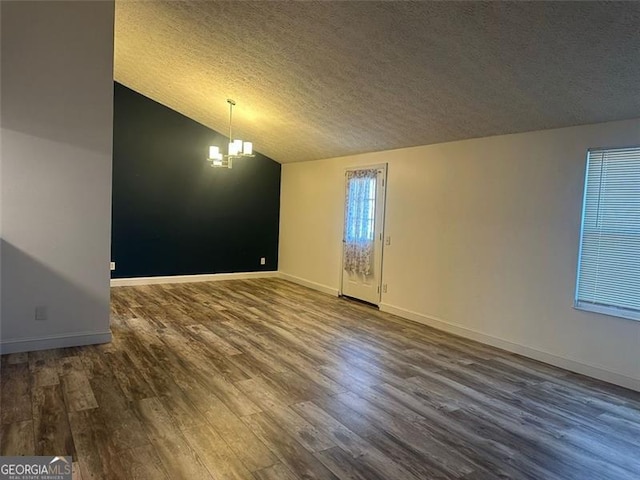 empty room with a chandelier, wood-type flooring, a textured ceiling, and vaulted ceiling