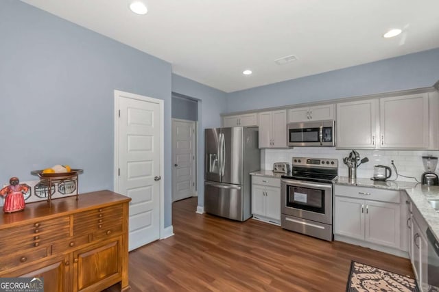 kitchen with light stone countertops, appliances with stainless steel finishes, backsplash, dark hardwood / wood-style floors, and white cabinetry