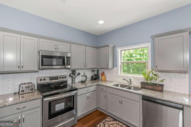 kitchen featuring dark hardwood / wood-style flooring, light stone counters, stainless steel appliances, sink, and gray cabinets