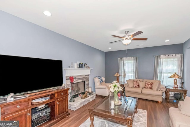 living room with a stone fireplace, ceiling fan, and wood-type flooring