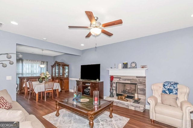 living room featuring a stone fireplace, ceiling fan, and dark hardwood / wood-style floors