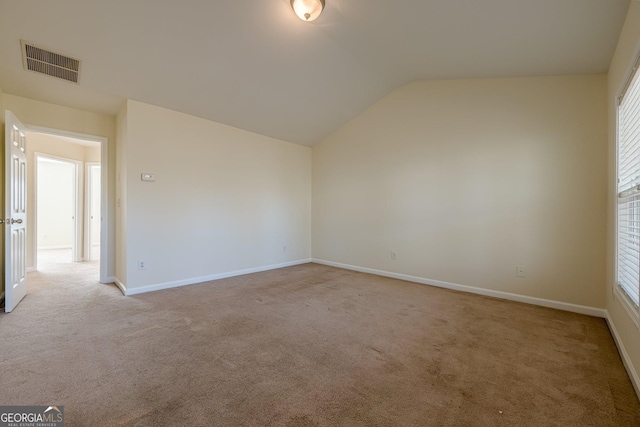 empty room with visible vents, lofted ceiling, light colored carpet, and baseboards