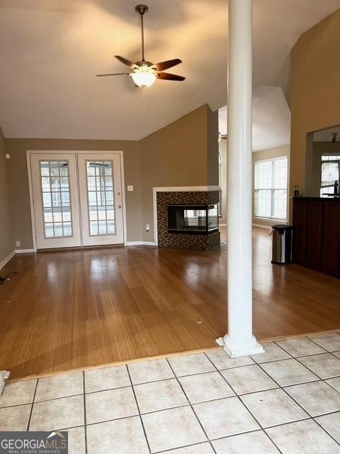 unfurnished living room featuring ornate columns, ceiling fan, light tile patterned flooring, and lofted ceiling