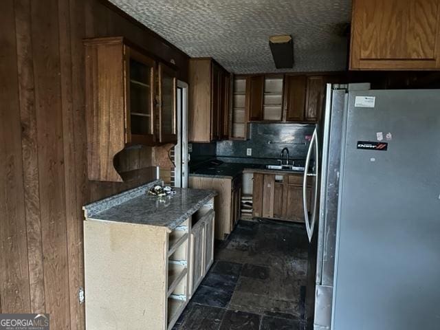 kitchen featuring wooden walls, sink, and stainless steel refrigerator