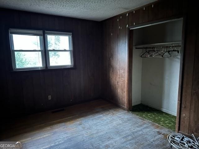 unfurnished bedroom featuring light wood-type flooring, a textured ceiling, a closet, and wood walls