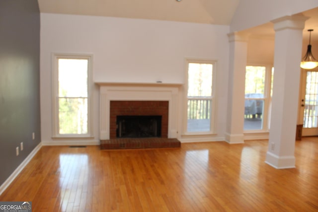 unfurnished living room featuring hardwood / wood-style floors, decorative columns, a brick fireplace, and lofted ceiling