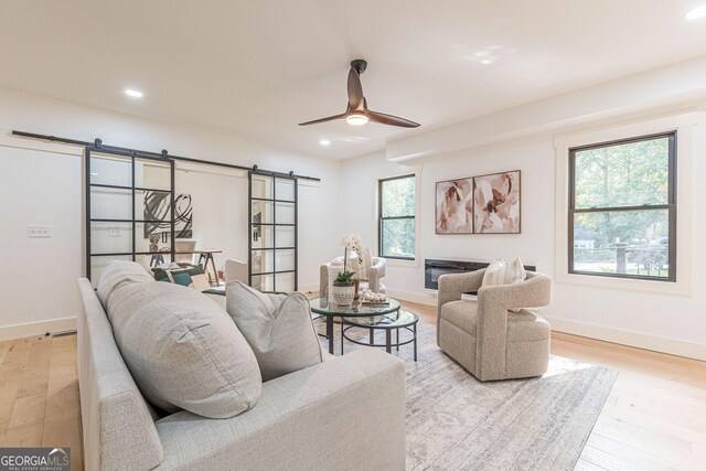 living room with ceiling fan, a barn door, and light hardwood / wood-style flooring