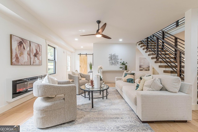 living room featuring a barn door, ceiling fan, and light hardwood / wood-style flooring