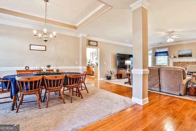 dining area with decorative columns, crown molding, light hardwood / wood-style floors, a fireplace, and ceiling fan with notable chandelier