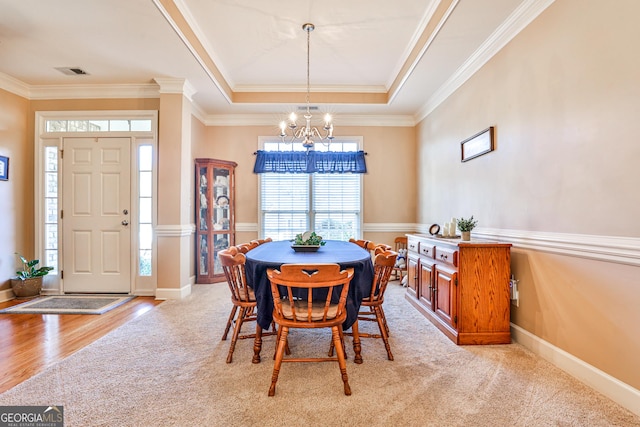 dining room with a notable chandelier, a raised ceiling, light colored carpet, and crown molding