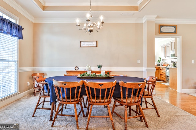 dining space featuring a raised ceiling, light hardwood / wood-style floors, an inviting chandelier, and ornamental molding