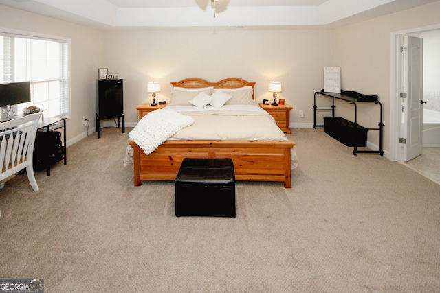 carpeted bedroom featuring a raised ceiling and ensuite bath