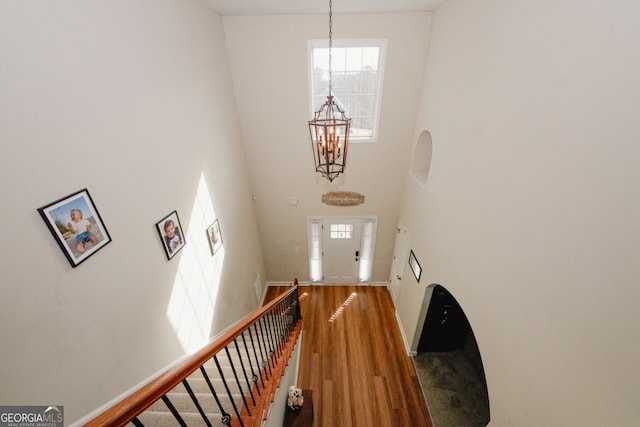 stairway with wood-type flooring, a towering ceiling, and an inviting chandelier