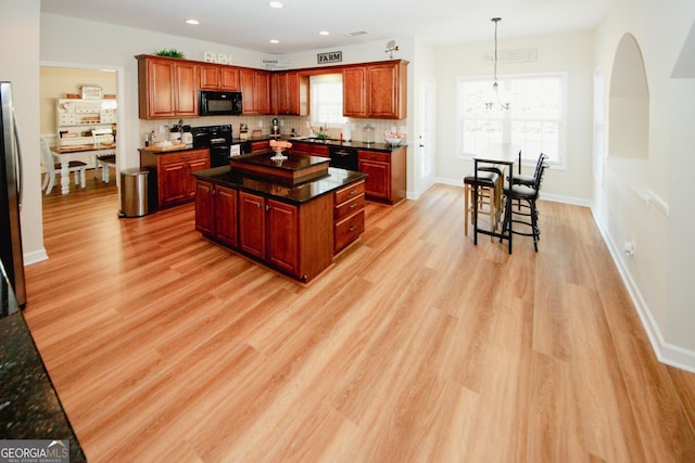 kitchen featuring pendant lighting, a center island, black appliances, sink, and light hardwood / wood-style flooring