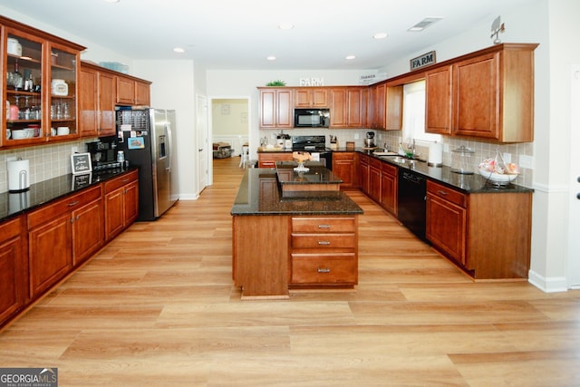 kitchen with sink, light hardwood / wood-style flooring, dark stone counters, a kitchen island, and black appliances