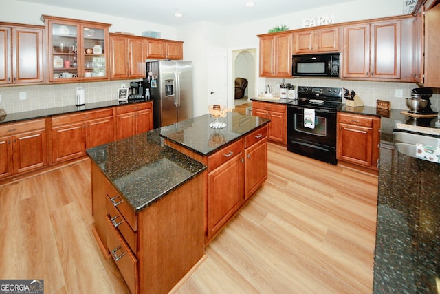 kitchen with black appliances, a center island, dark stone countertops, and light wood-type flooring