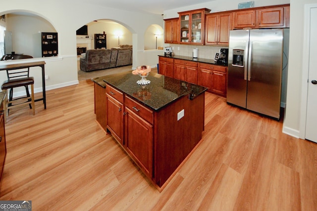 kitchen with tasteful backsplash, dark stone counters, stainless steel fridge with ice dispenser, a center island, and light hardwood / wood-style floors