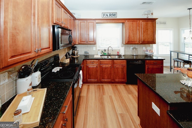 kitchen featuring black appliances, sink, hanging light fixtures, dark stone countertops, and light hardwood / wood-style floors