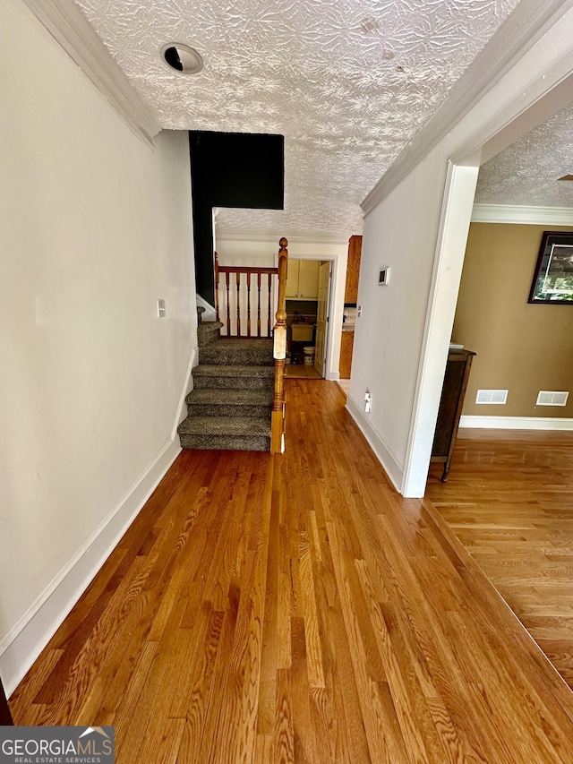 hall with light hardwood / wood-style floors, a textured ceiling, and ornamental molding