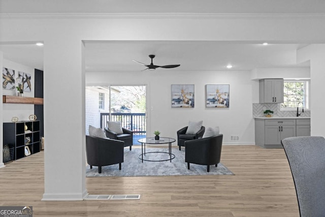 living room featuring ceiling fan, light wood-type flooring, and crown molding